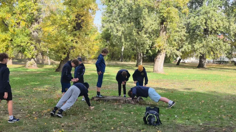 Jugendliche in dunkelblauen Vereinsjacken machen auf einer Wiese im Park Liegestütze an einem Baumstumpf, andere schauen zu.