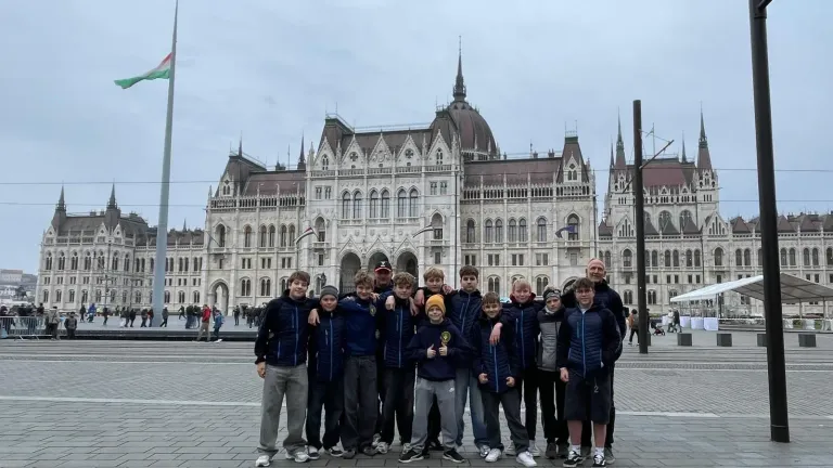 Gruppe Jugendlicher in dunkelblauen Vereinsjacken mit zwei Betreuern vor dem Parlamentsgebäude in Budapest